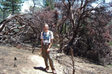 Bill B. stands before fire-blackened manzanita trees.